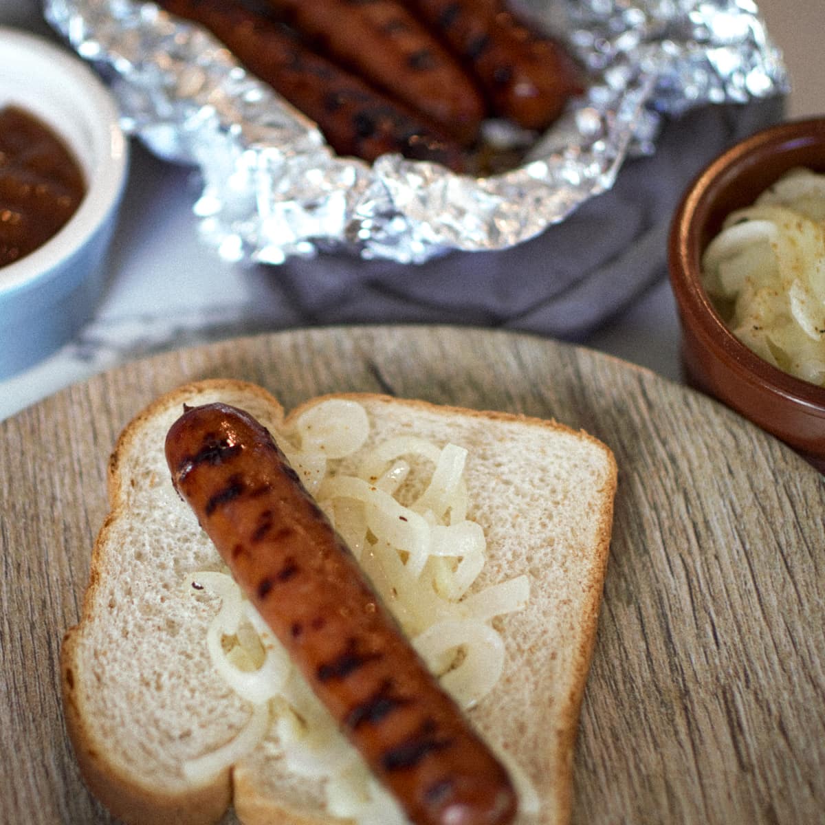 Grilled sausage on a slice of white bread with seasoned onions.