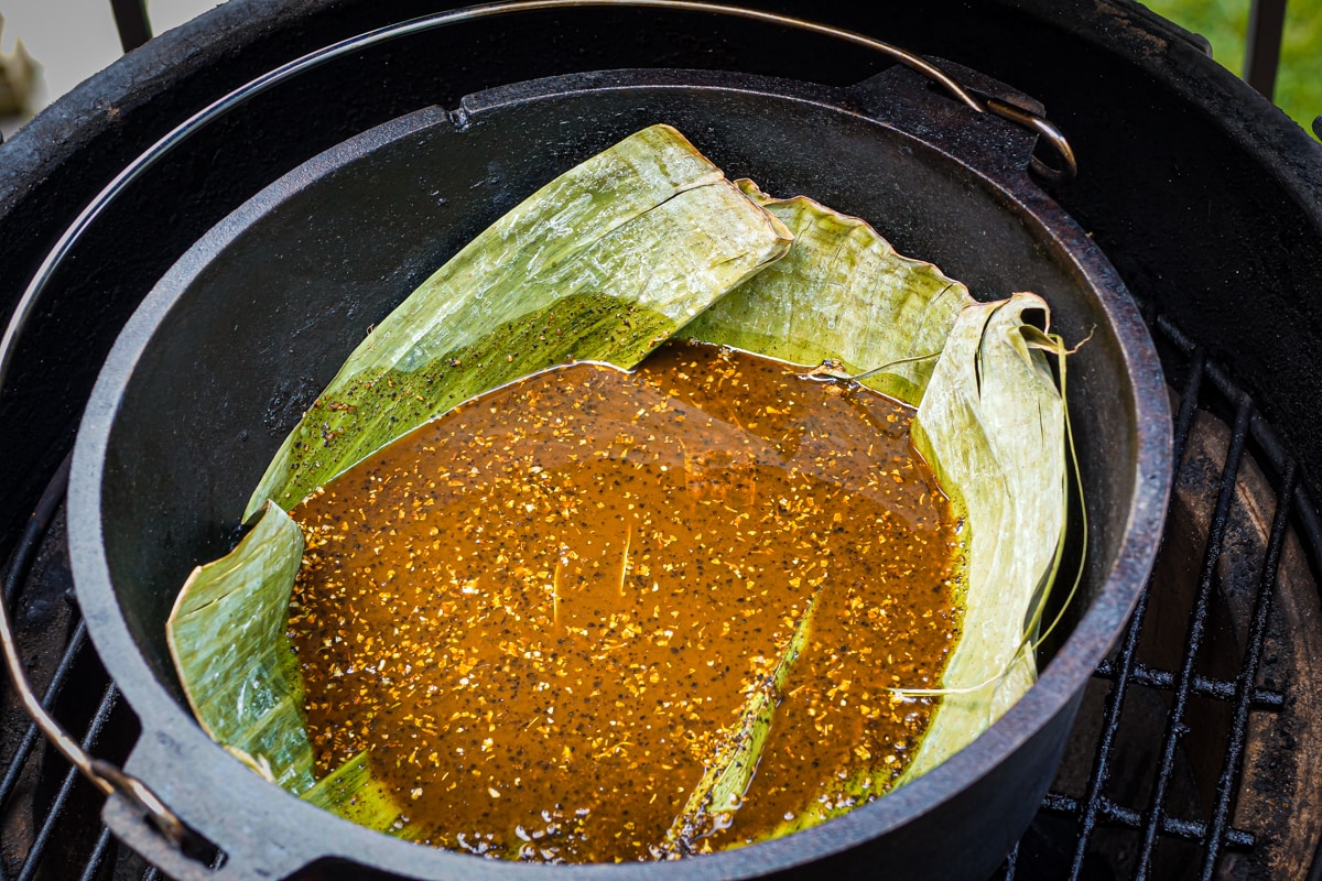 Dutch oven on a Big Green Egg.  Lined with banana leaves and containing chili braising liquid.