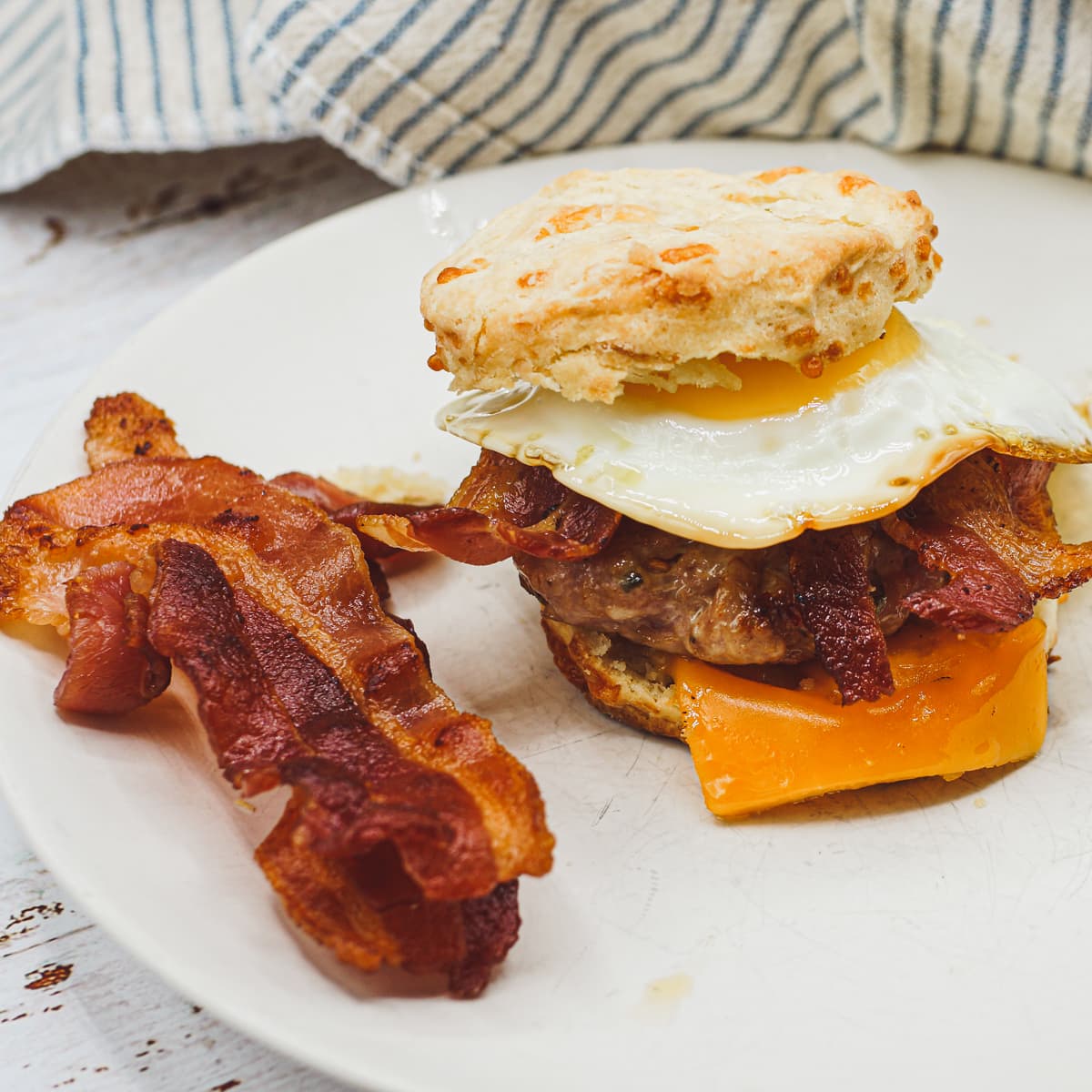 Breakfast sandwich served with a side of bacon.