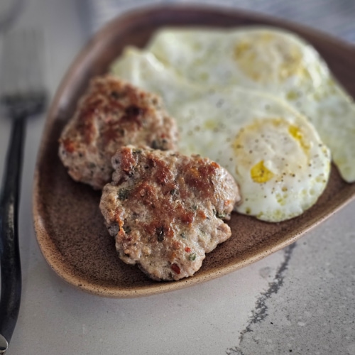 Breakfast sausage with fresh sage served on a plate with over easy eggs.