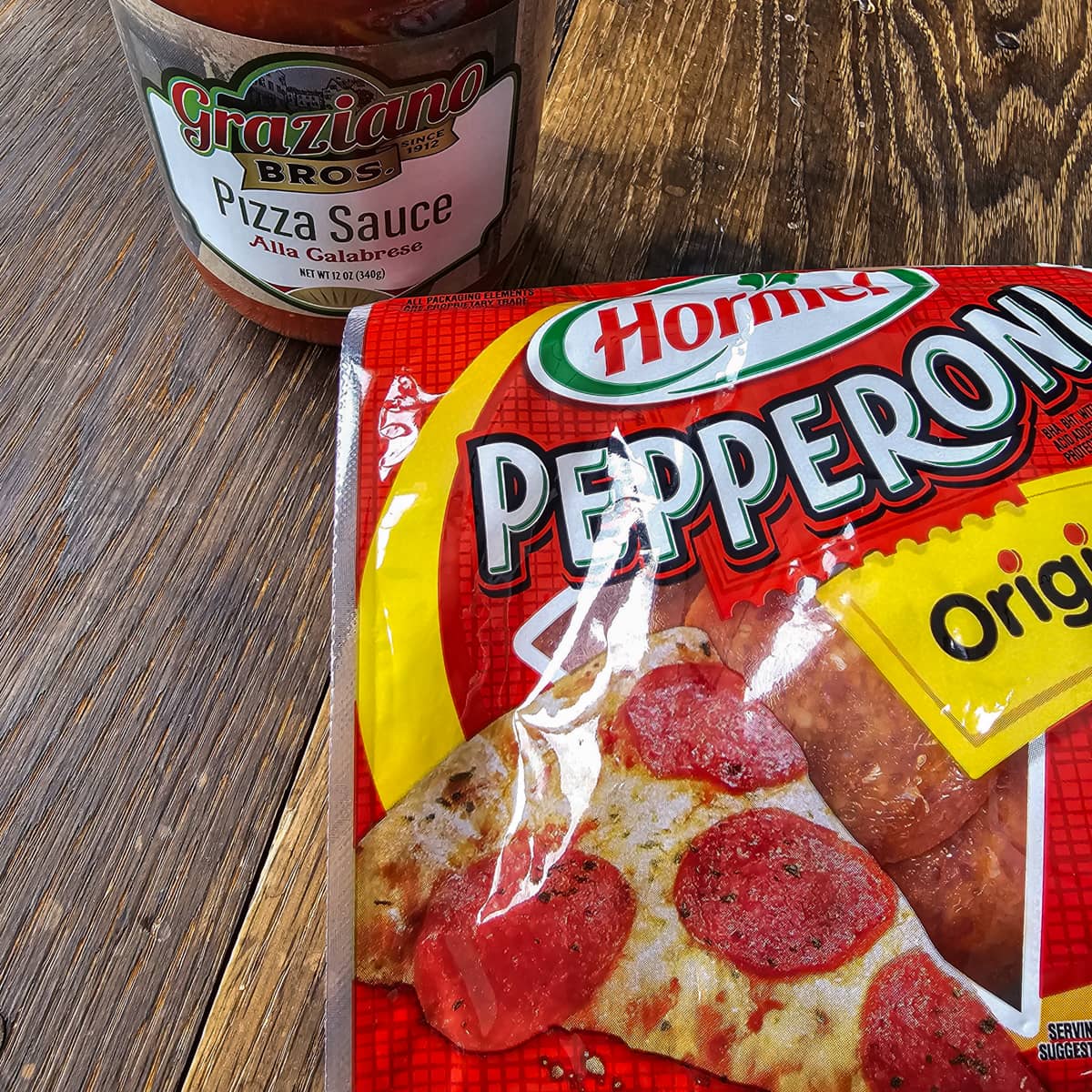 A jar of pizza sauce and pepperonis on a table.