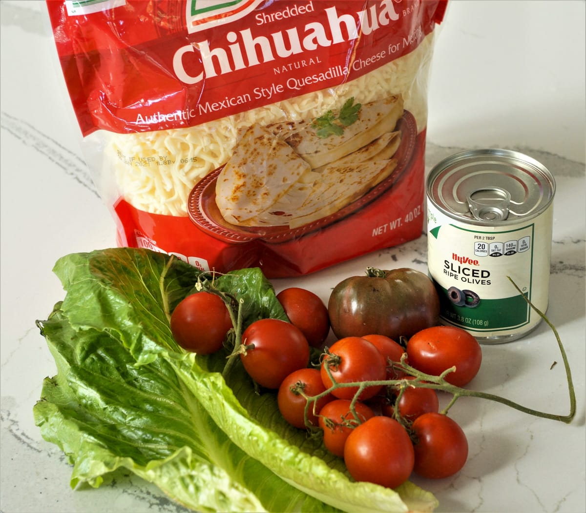 Tomatoes, cheese, lettuce and olives on a countertop.