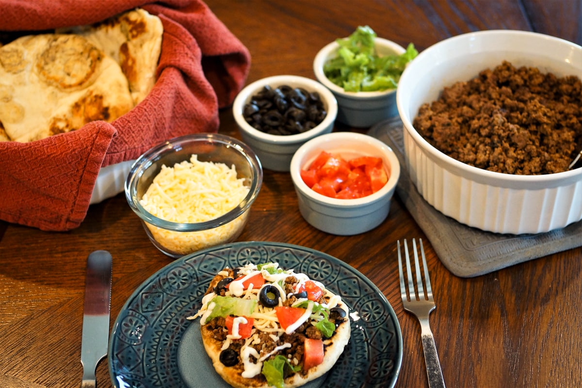 Navajo fry bread with buffalo meat and assorted toppings on a table.