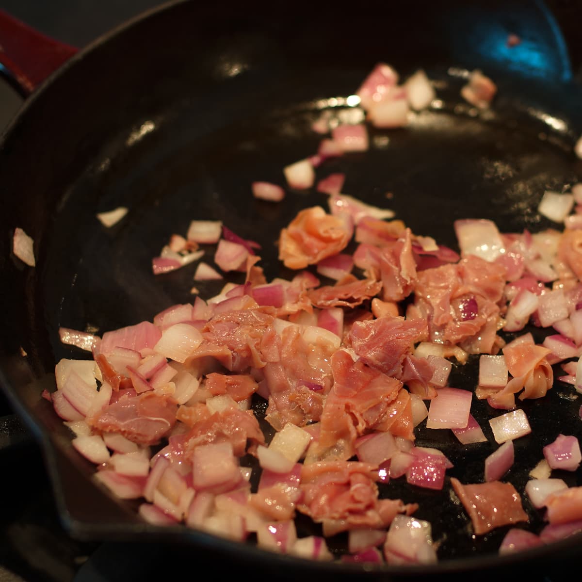Onion and prosciutto cooking in a cast iron pan. 