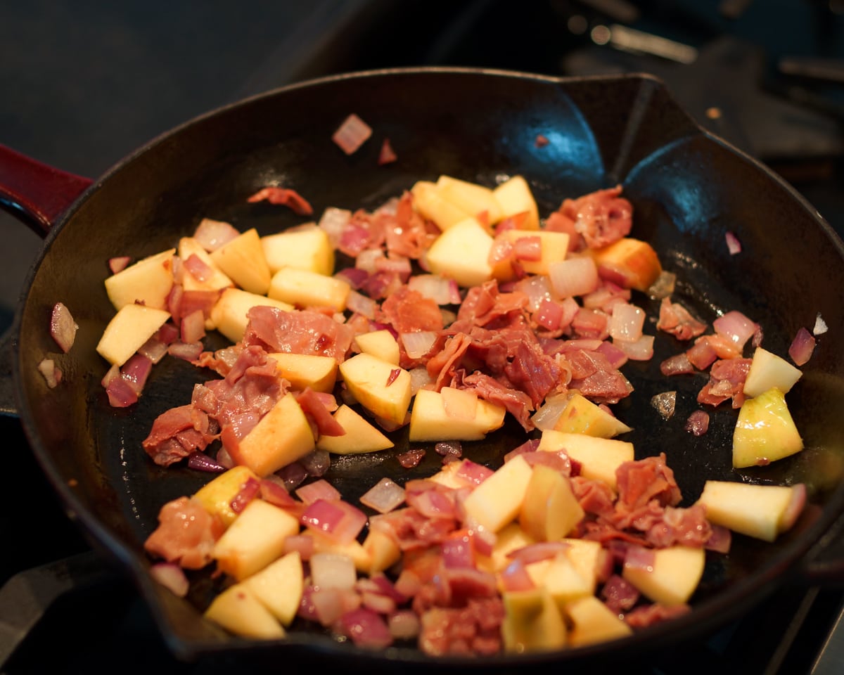 Apples and prosciutto cooking in a pan.