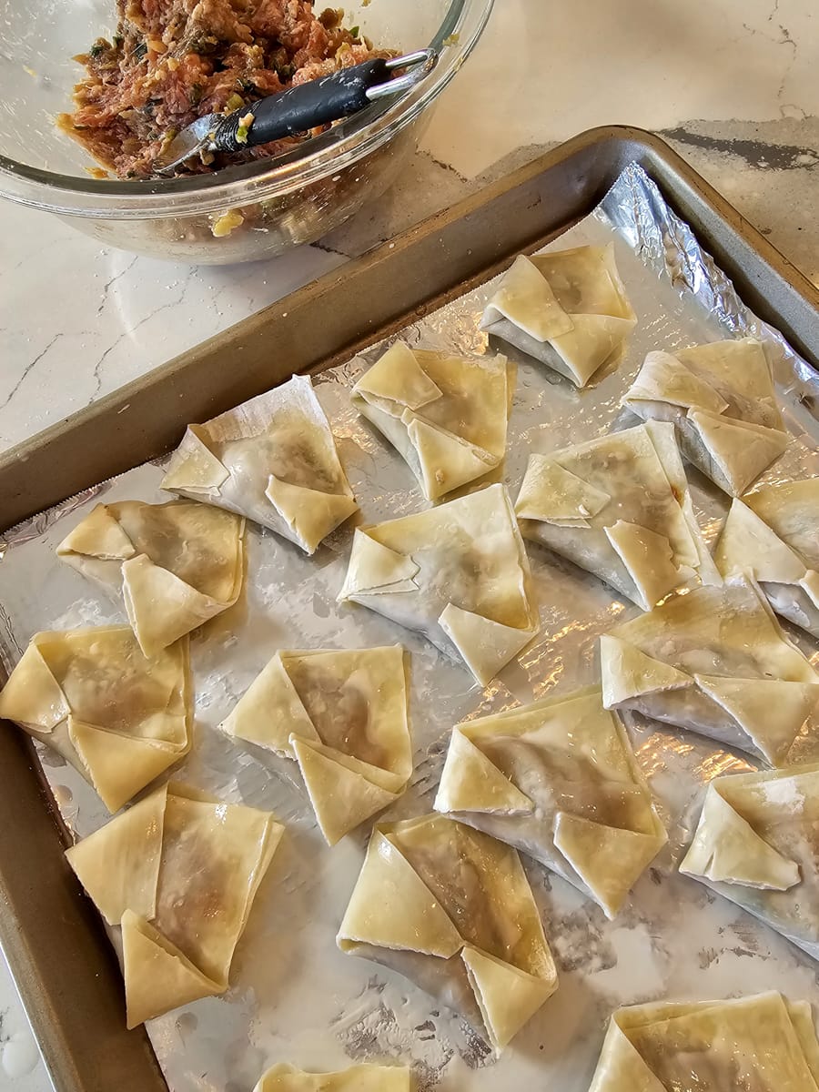 Filling wonton wrappers with a sausage, ginger, and water chestnut filling.