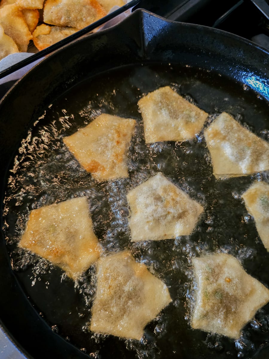 Sausage filled wontons frying in a cast iron pan.