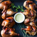 Roasted Peruvian half chickens on a plate with homemade aji verde sauce.