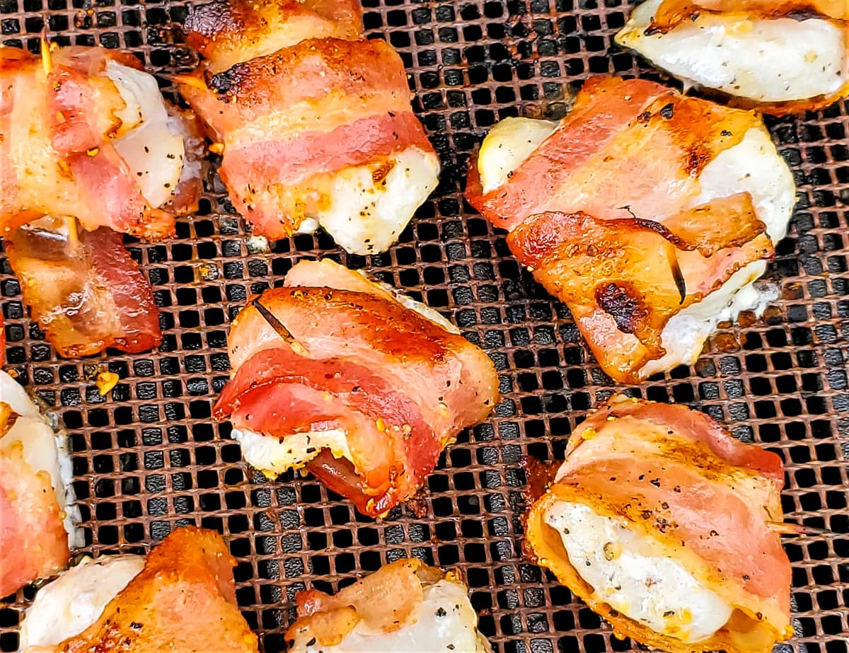 Bacon wrapped halibut cheeks on a grill.