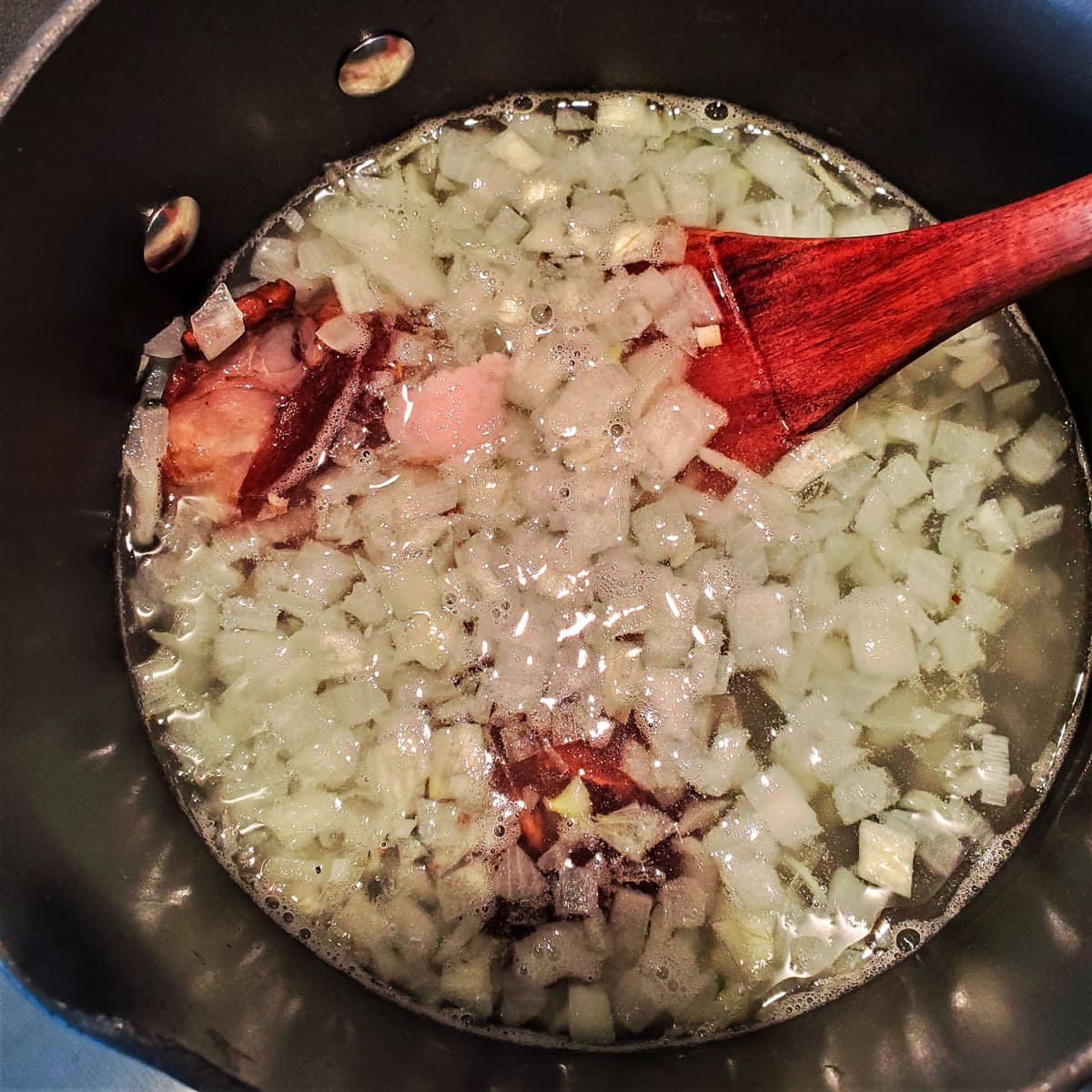 Diced onion and ham hocks simmering in a pot of water.
