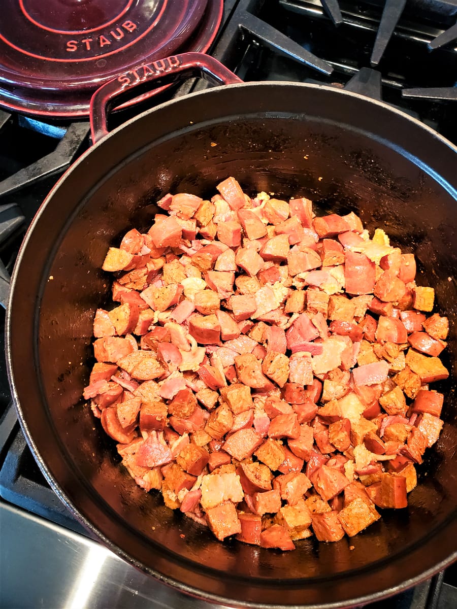 Bacon and diced sausages cooking in a Dutch Oven.