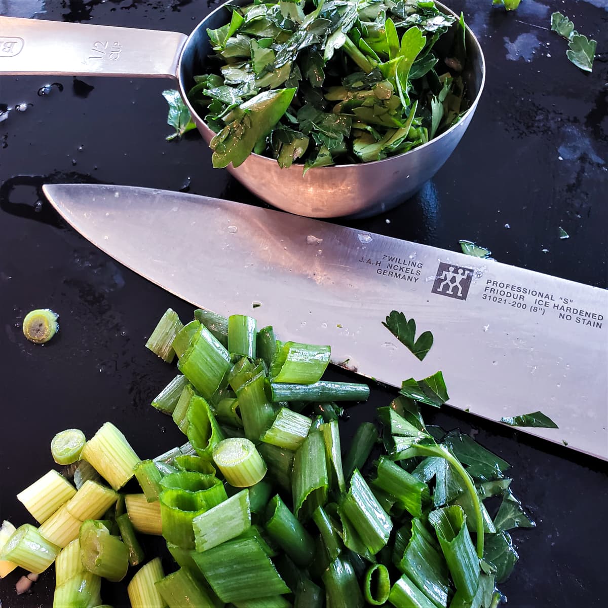 ½ cup measuring cup with parsley and diced green onion on a cutting board.