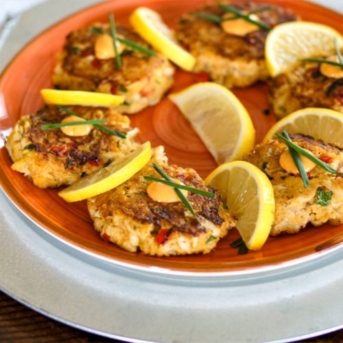 Fried Lump Crab Cakes topped with Sriracha Aioli and chives with lemon slices.