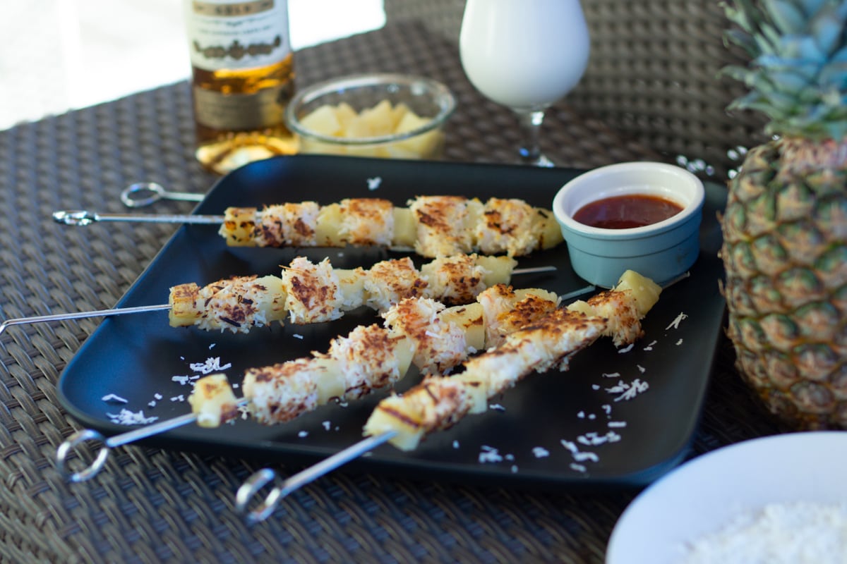 Pina colada style coconut shrimp skewers on a black plate.