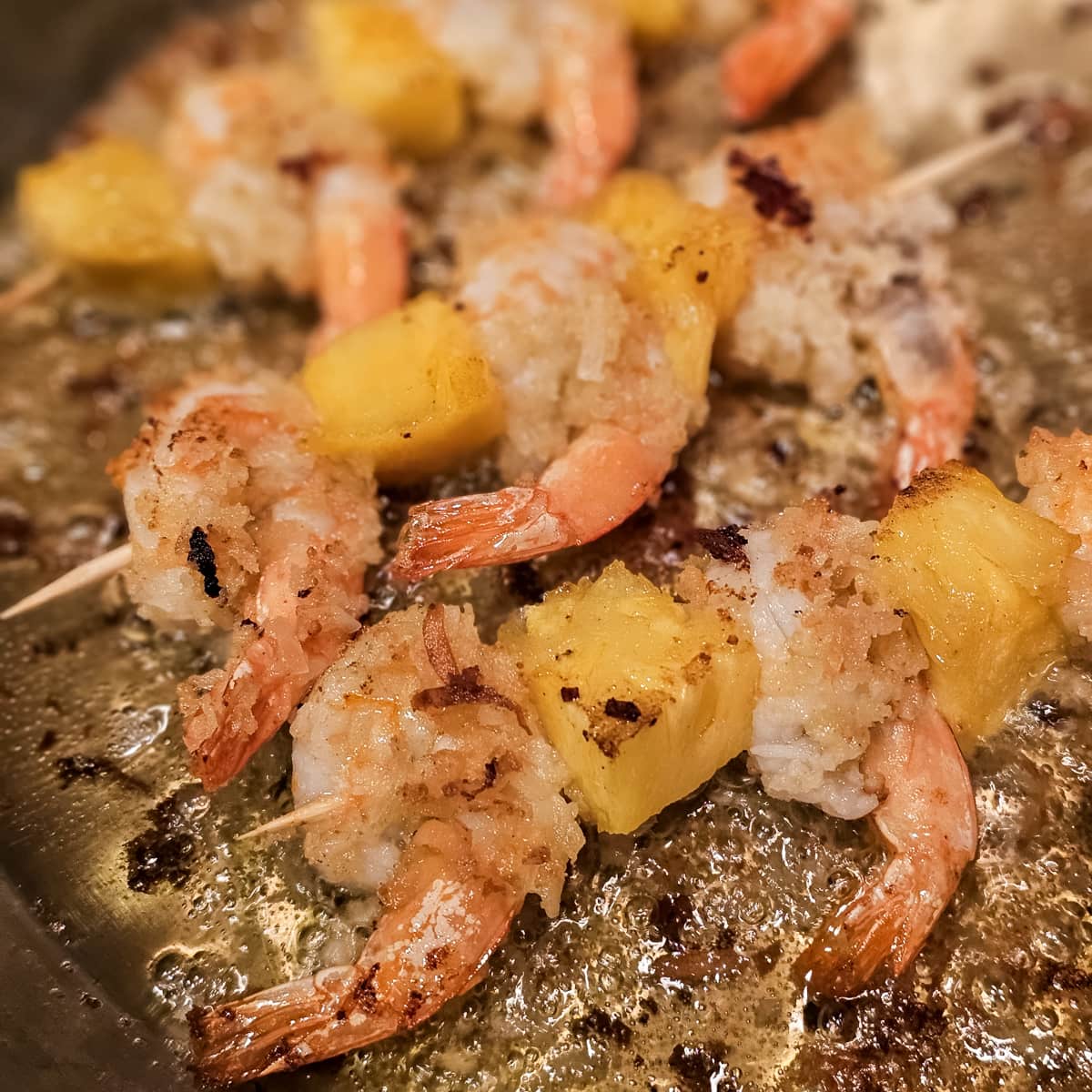 Pina colada style shrimp skewers cooking in a skillet.