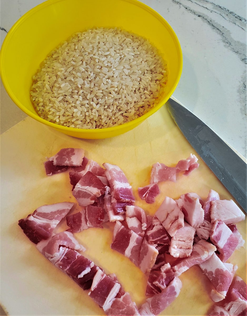 Bowl of rice on a cutting board with diced bacon.