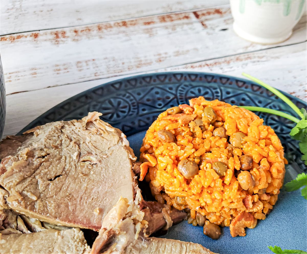 Arroz con gandules in a bowl next to a plate of smoked pernil.