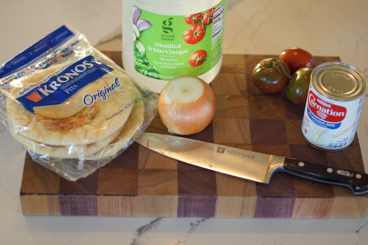 pitas, tomato, onion, and white vinegar on a cutting board.