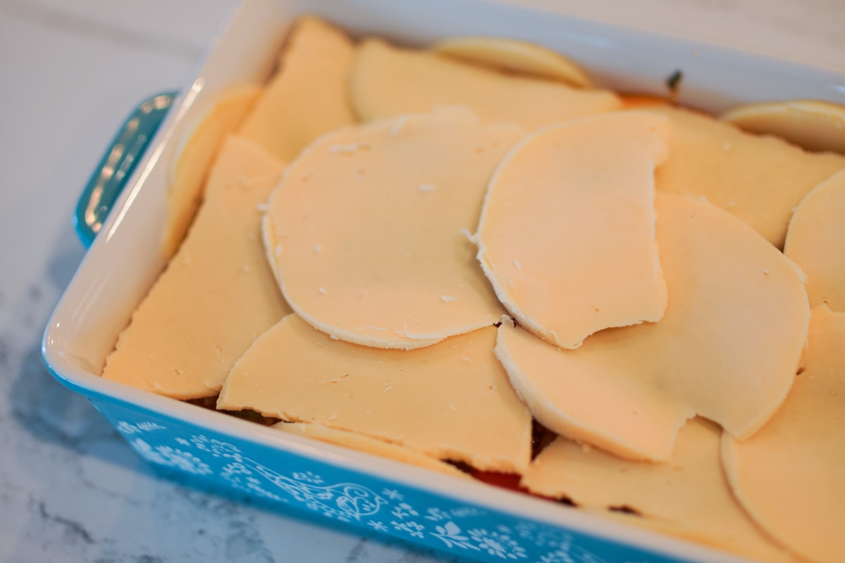 Keshi Yena in a casserole dish topped with cheese, ready for the oven.