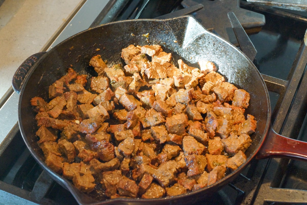 Carne asada cooking in a Staub cast iron pan.