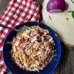 Bowl of Jalapeno Coleslaw with Bacon aioli on a table with red onion and jalapenos.