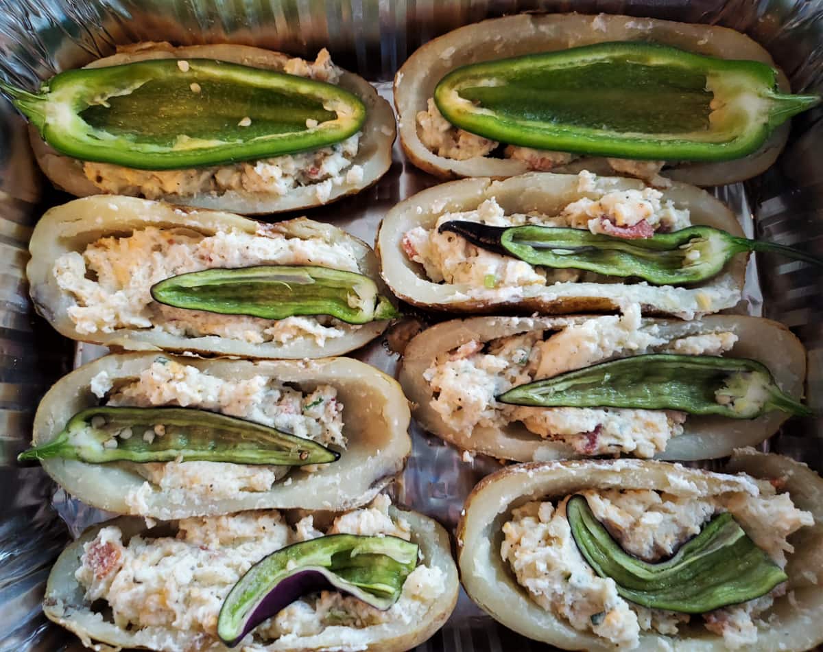 Twice baked potato boats in a pan with halved jalapenos.