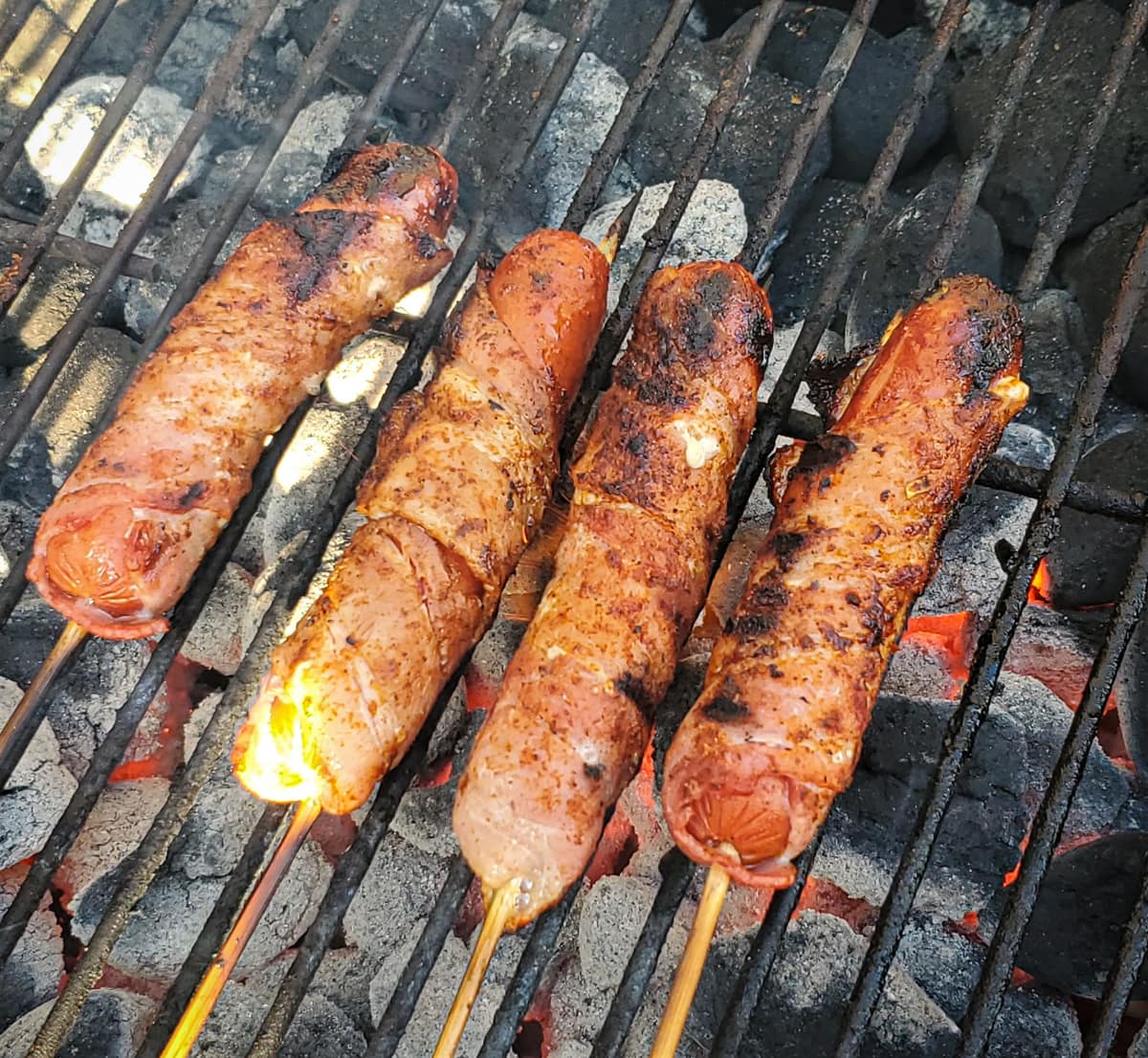 Bacon wrapped hotdogs on a grill.