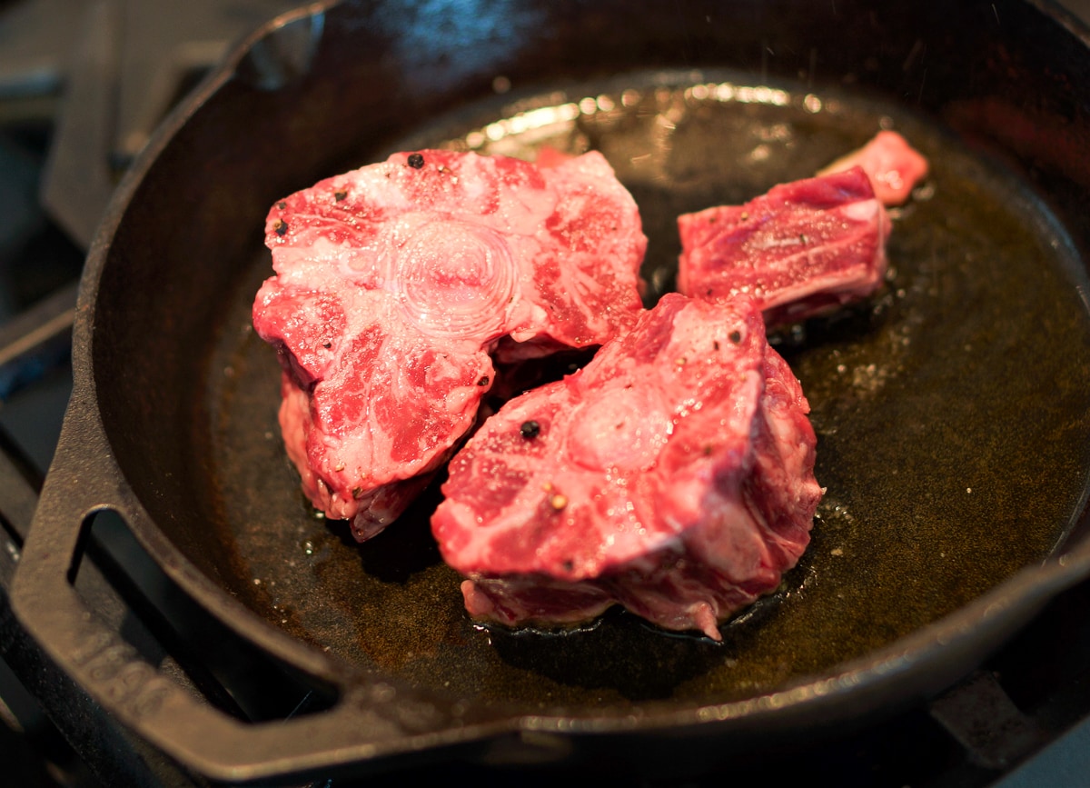 Oxtails browning in a cast iron pan.