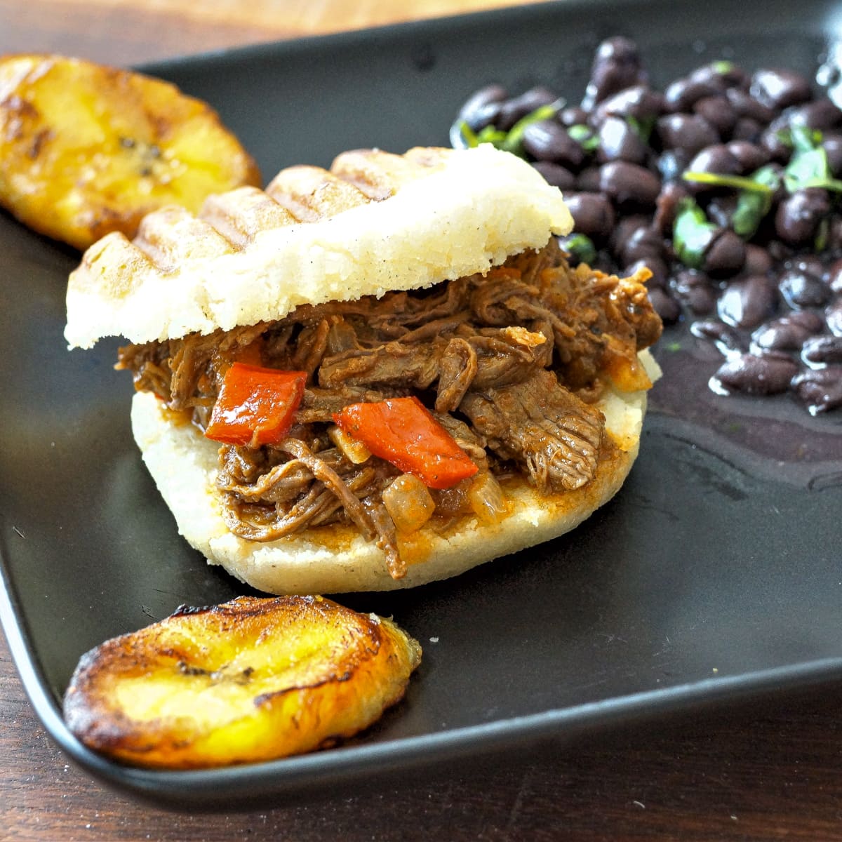 Shredded carne mechada served on an arepa with black beans and plantains.