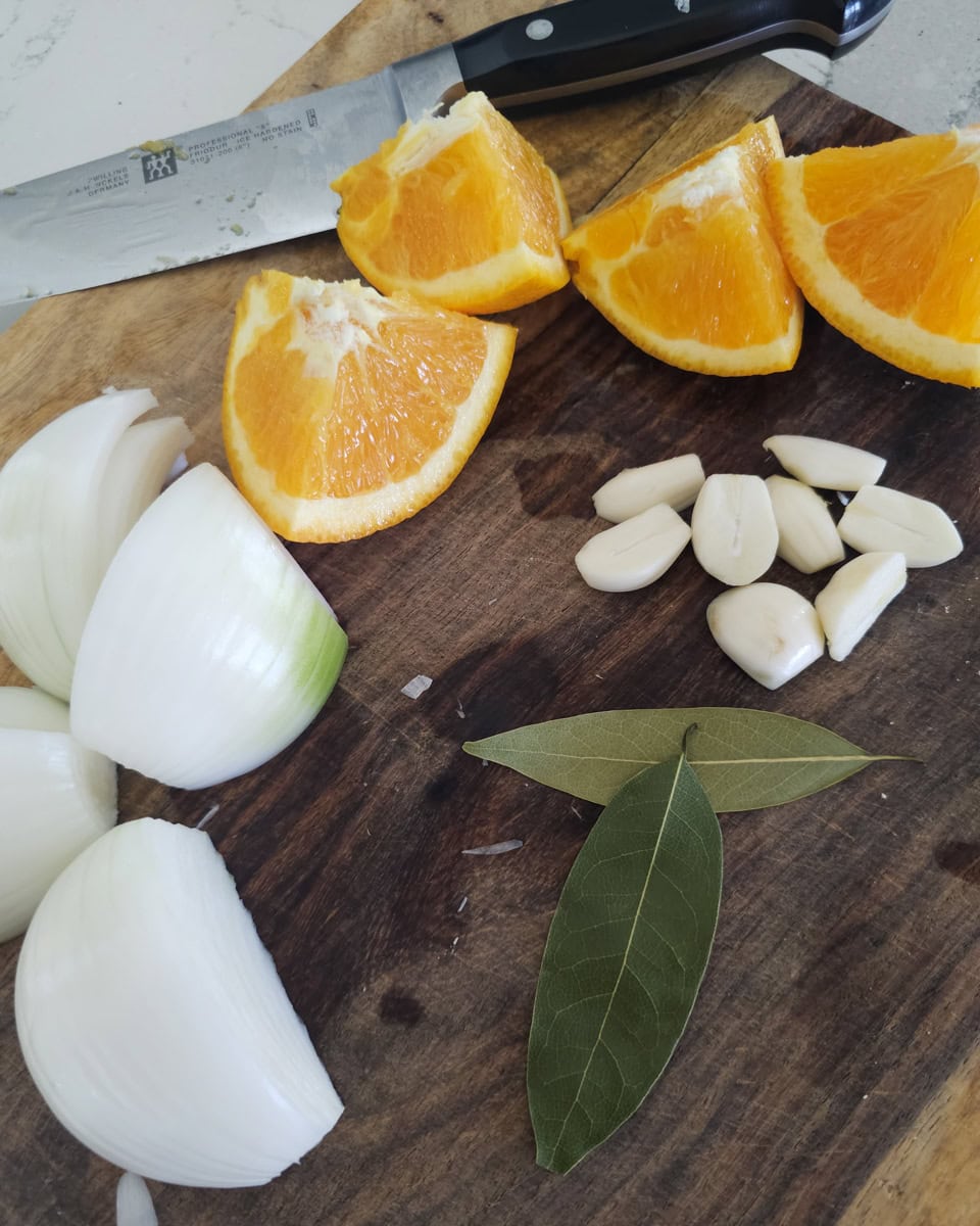 Quartered white onion and oranges with garlic cloves on a cutting board.