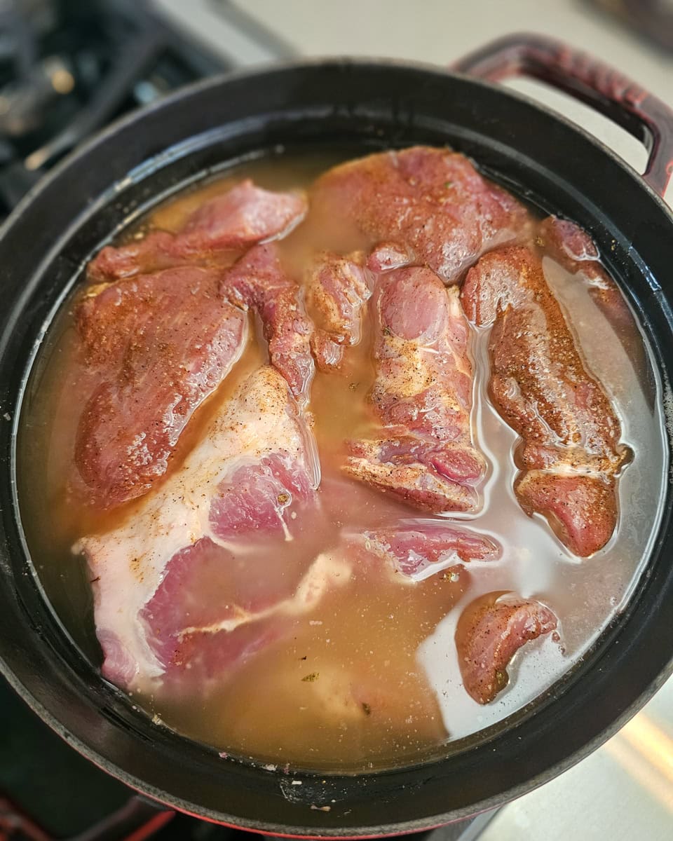 Pork carnitas cooking in lard in a Dutch oven.