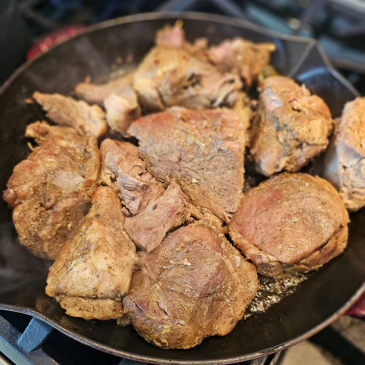 Chunks of fat cooked carnitas frying in a pan.