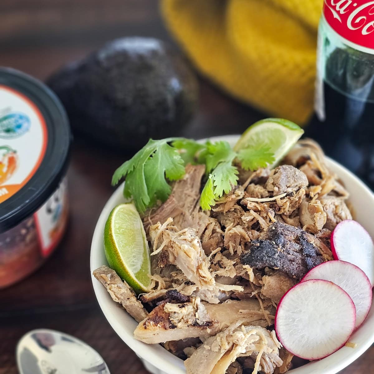 Bowl of Carnitas Michoacan served with salsa, avocado, and lime wedges.