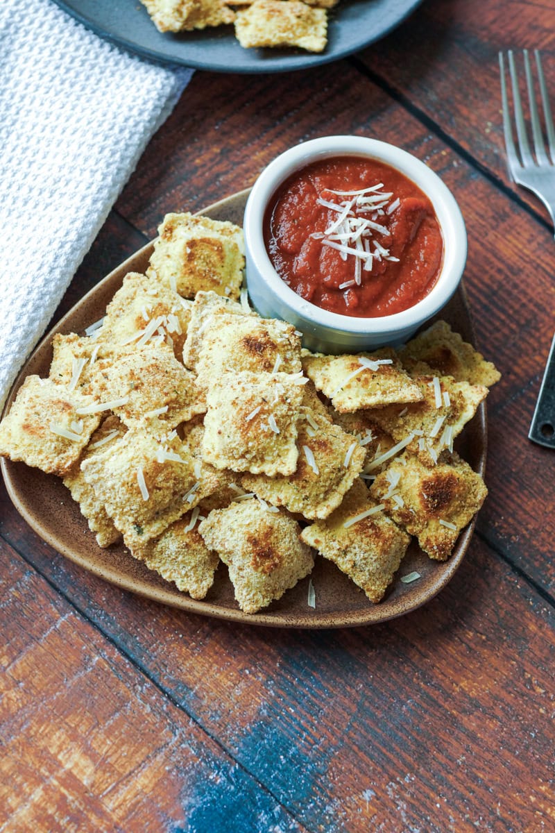 Griddle fried breaded ravioli on a plate with marinara sauce..