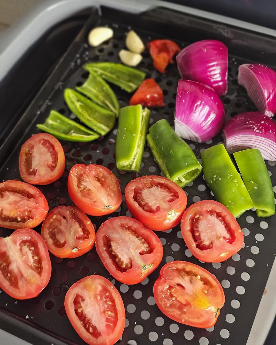 Salted and halved peppers and tomatoes on a roasting pan.