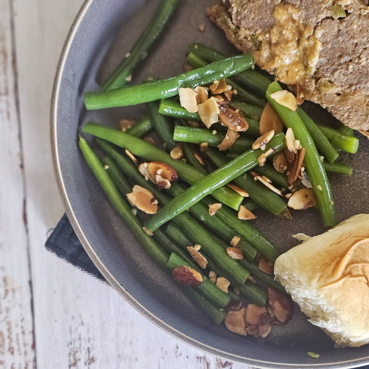 Haricots Verts Amandine served with meatloaf on a plate.