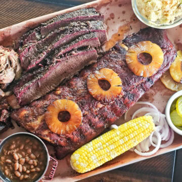 A tray of al pastor flavored ribs, brisket, corn, and beans.