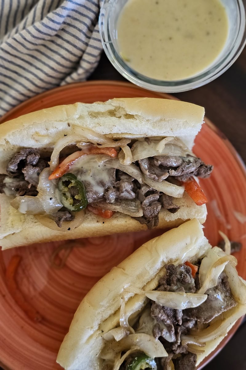 Plate with 2 carne asada Mexican cheesesteak sandwiches, served with white cheese dip.