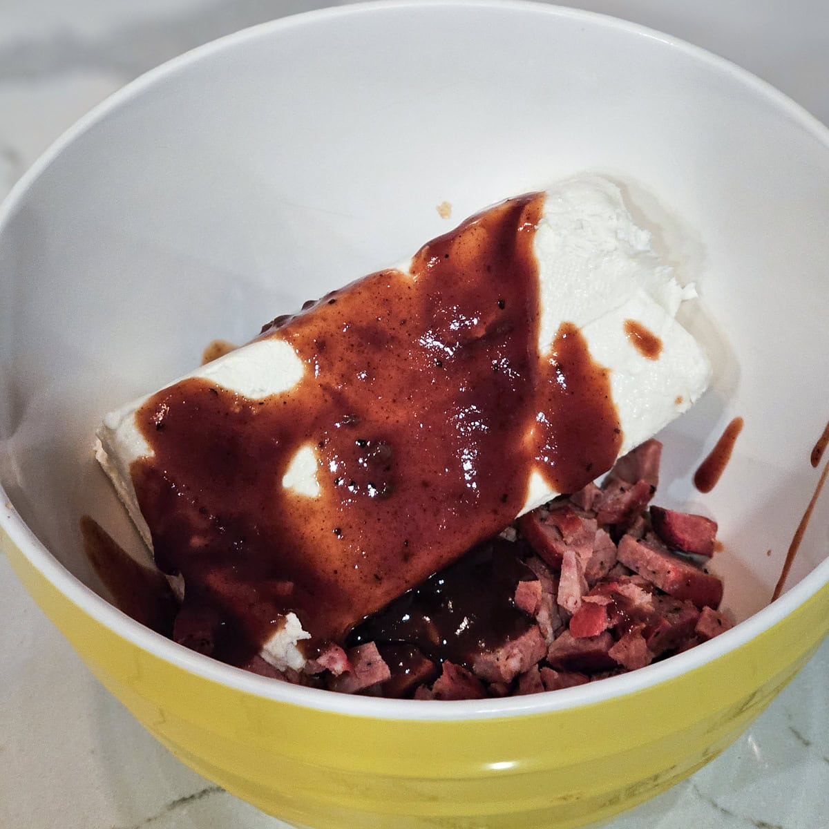 Mixing cream cheese with BBQ sauce and hot link sausage.
