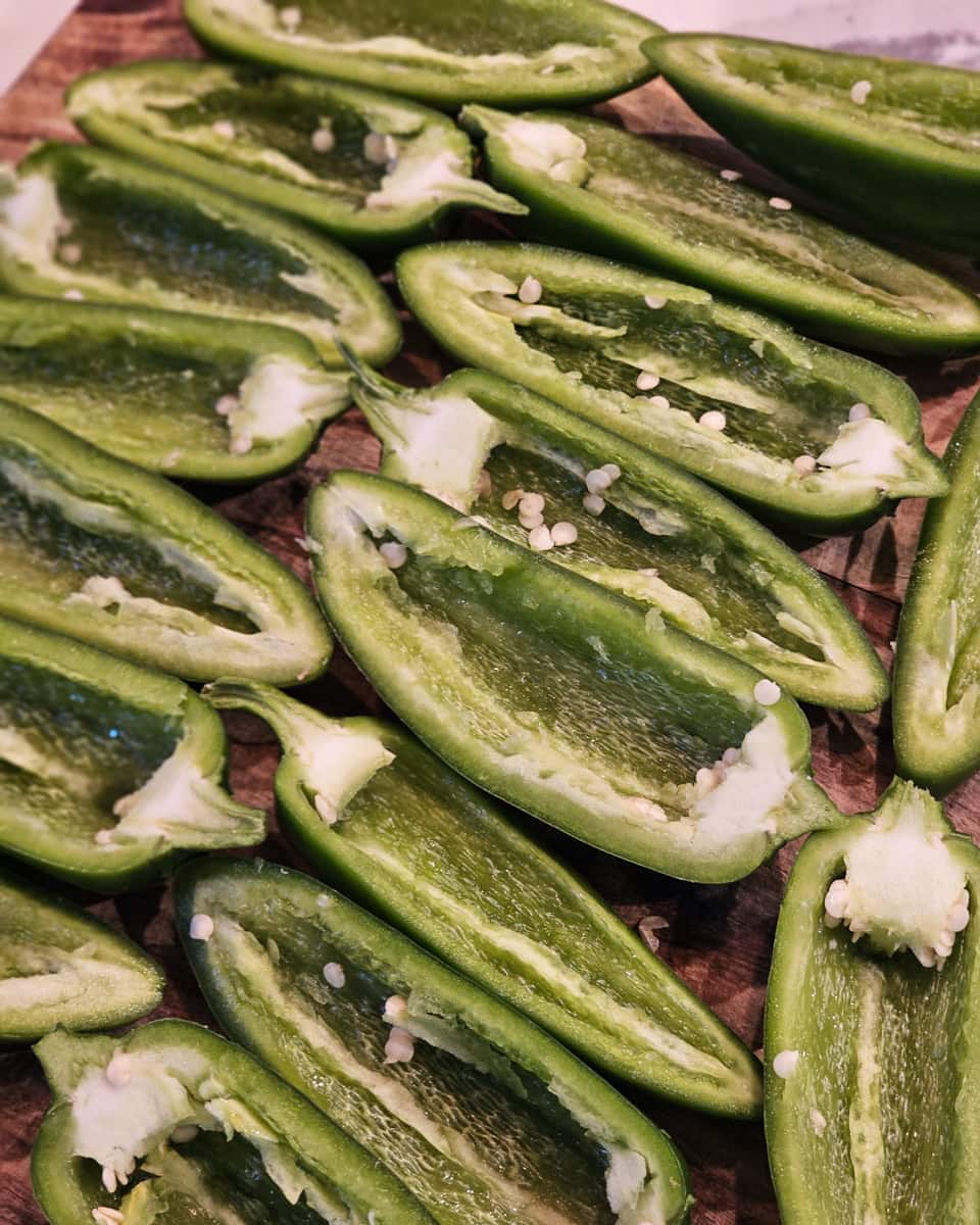 Halved and deseeded jalapenos on a cutting board.