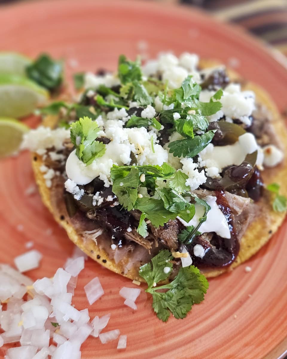 Smoked BBQ pulled pork tostadas with refried beans, sour creams, and BBQ sauce.