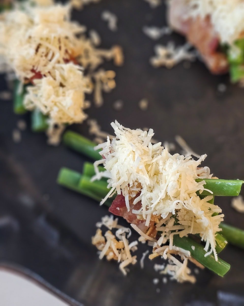 Shredded Gruyere cheese on top of bacon wrapped green bean bundles.