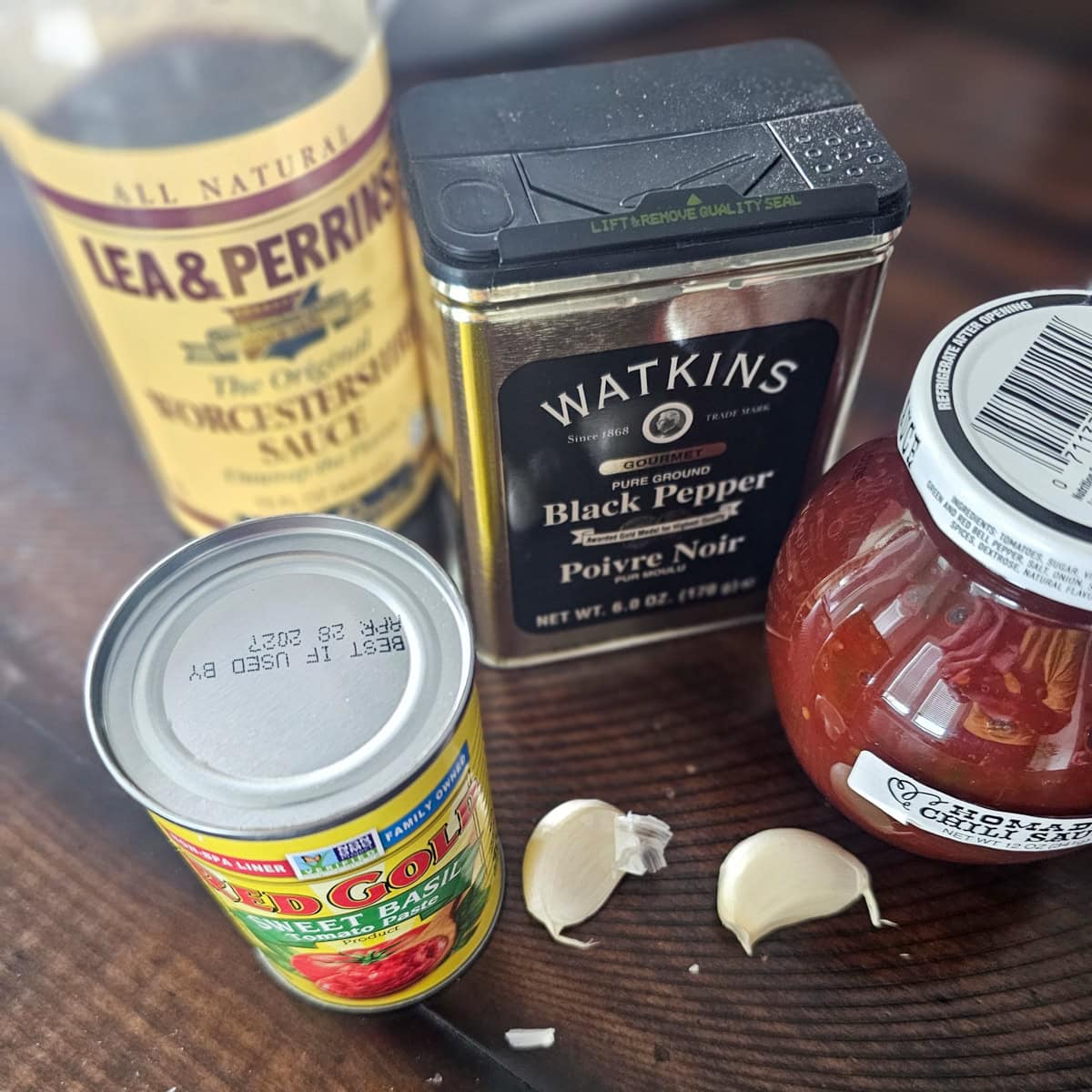 Chili sauce, garlic, Worcestershire sauce, tomato paste, and black pepper on a table.