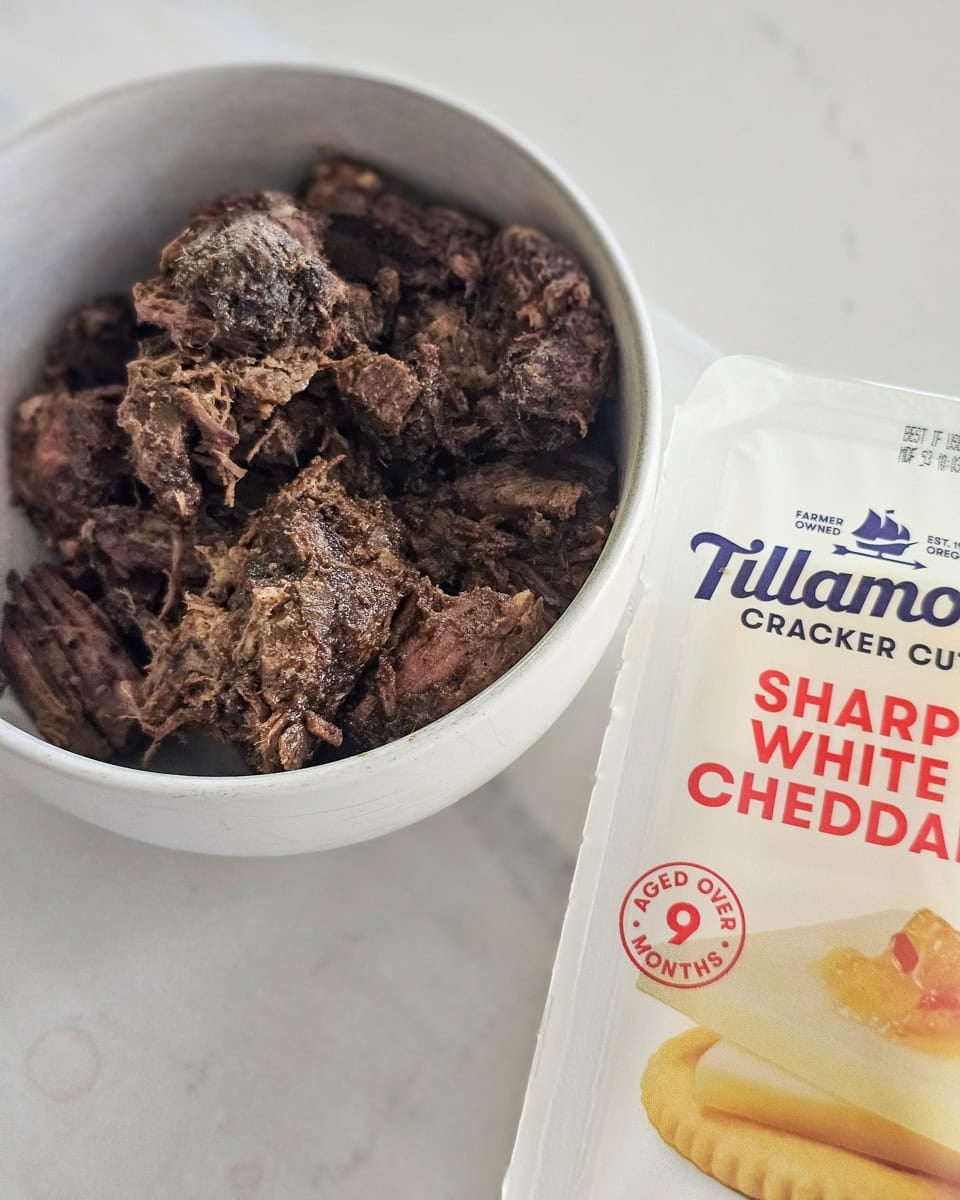 Bowl of chopped BBQ brisket and a package of sliced white cheddar cheese.