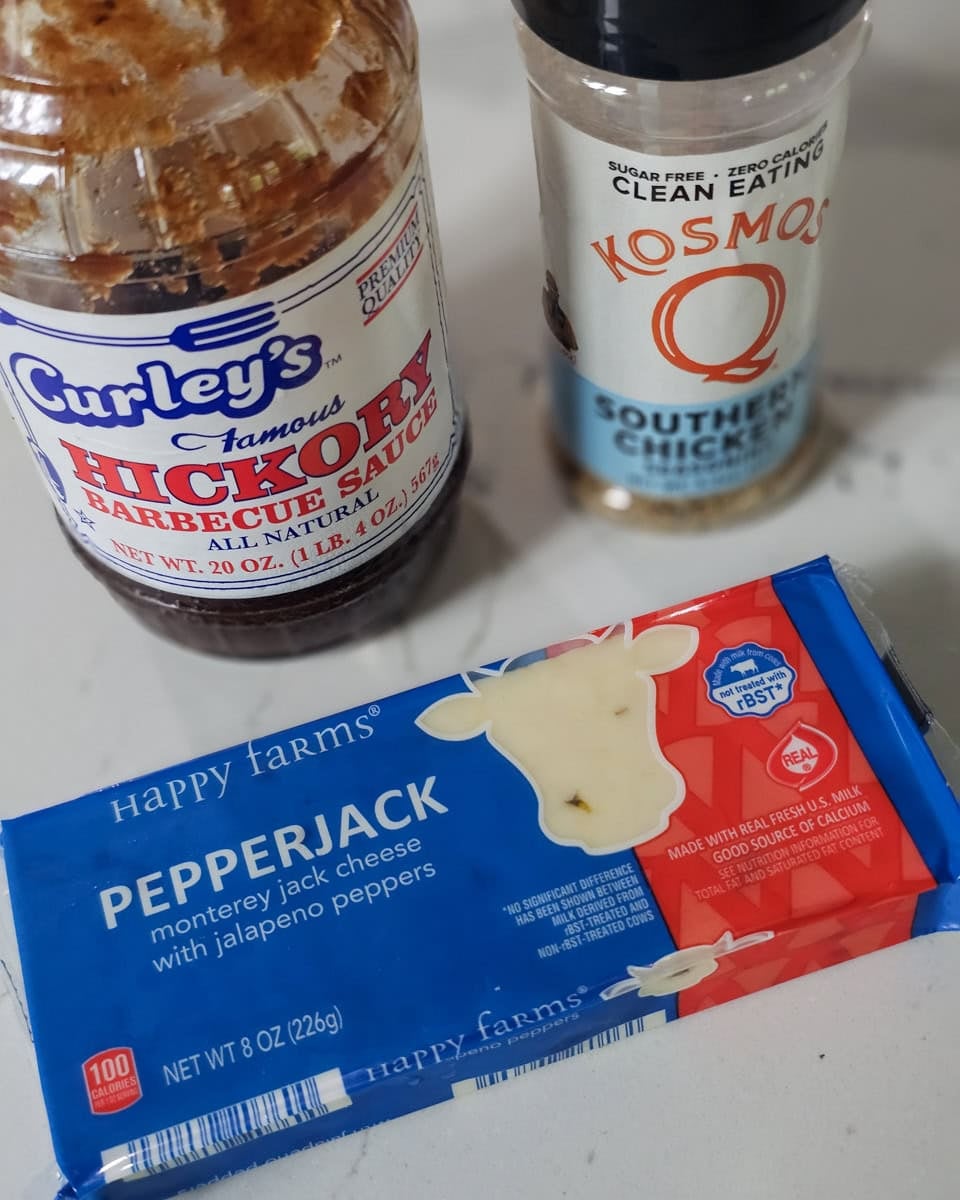 A bottle of BBQ sauce, package of pepper jack cheese and a shaker of chicken seasoning on a counter.