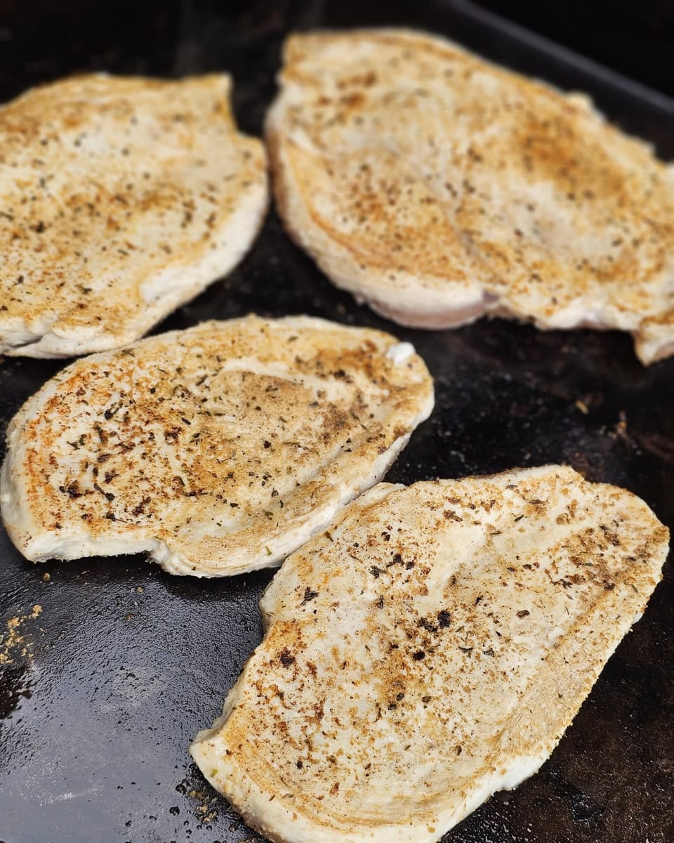 Seasoned chicken breast cooking on a flat top.