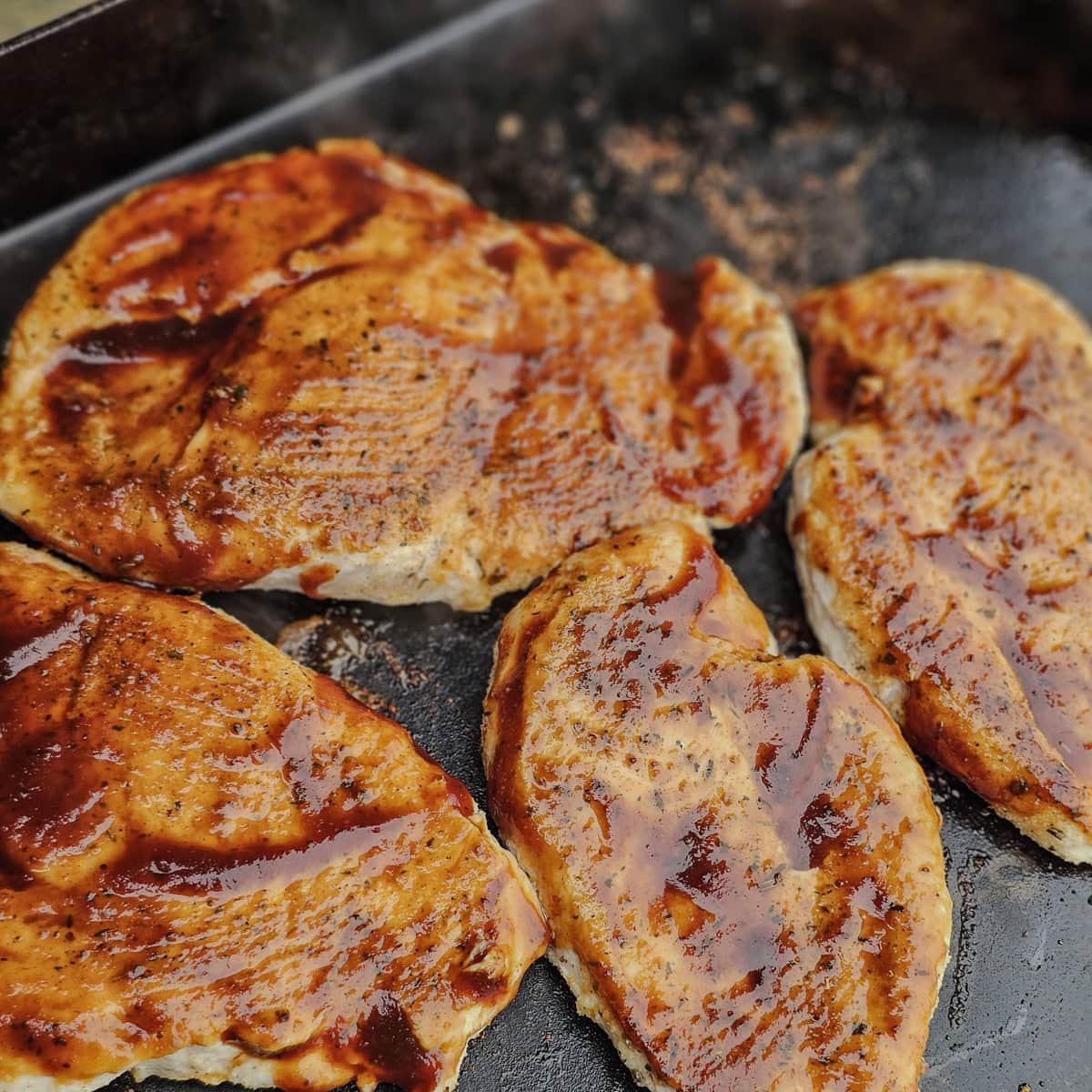 Chicken breasts basted with BBQ sauce, on a Blackstone.